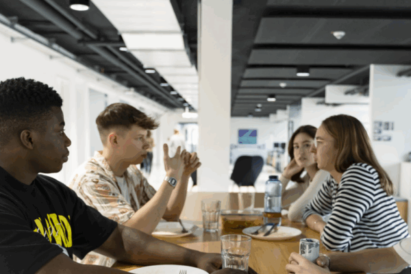 Junge Mitarbeitende genießen Mittagessen im Team – Austausch, Zusammenhalt und Wohlbefinden im Arbeitsalltag sichtbar.